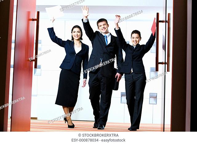 Portrait of successful business group standing at the door of conference hall with raised hands greeting their partners