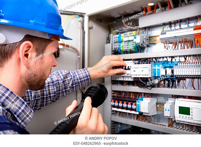 Close-up Of A Electrician Examining A Fuse Box With A Torch