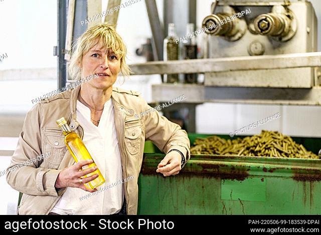 06 May 2022, Schleswig-Holstein, Norddeich: Maike Witthohn, canola farmer and miller, stands at her oil mill with a bottle of canola oil in her hand