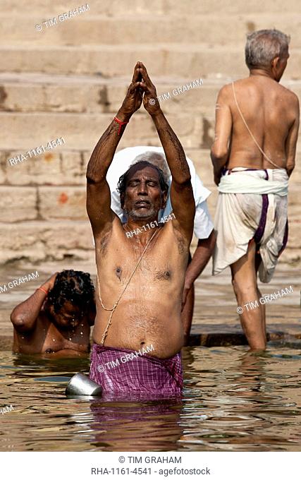 Indian Hindu man bathing and praying in the River Ganges by Kshameshwar Ghat in holy city of Varanasi, India