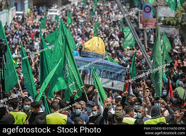 30 April 2021, Palestinian Territories, Jabalia: Supporters of the Palestinian Hamas Islamist movement wave flags and hold up a model of Jerusalem's Dome of the...