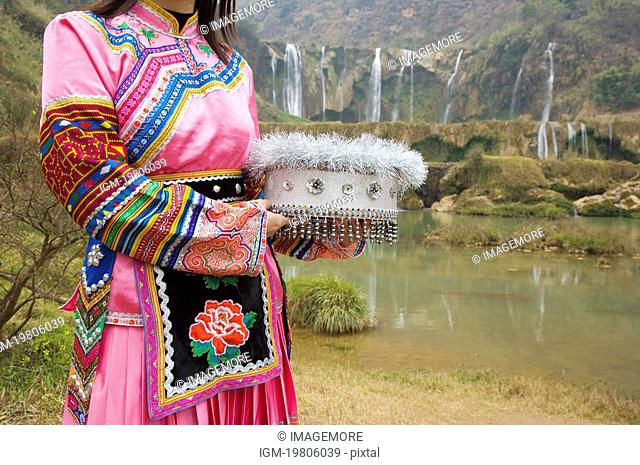 China, Yunnan Province, Luoping County, Buyi National Minority, Young woman in traditional clothing holding hat