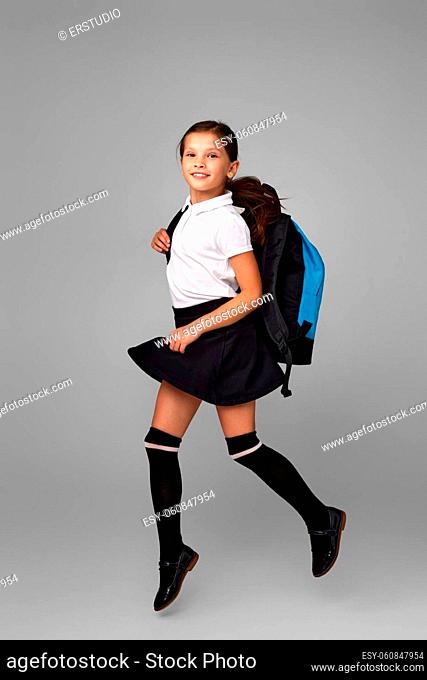 smiling little pupil jumping with blue backpack isolated on gray background. happy child is ready to learn. Back to school