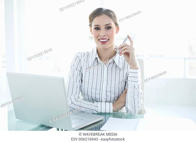 Lovely chic businesswoman sitting at her desk holding a pencil