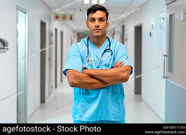 Portrait of mixed race male doctor smiling and standing in hospital corridor