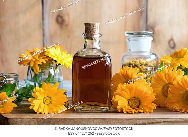 A bottle of calendula (marigold) tincture on a wooden table, with fresh and dry calendula flowers in the background