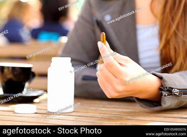 Close up of a woman hand showing supplement vitamin pill on a coffee shop terrace