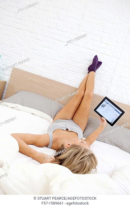 Young woman relaxing on her bed on her tablet computer