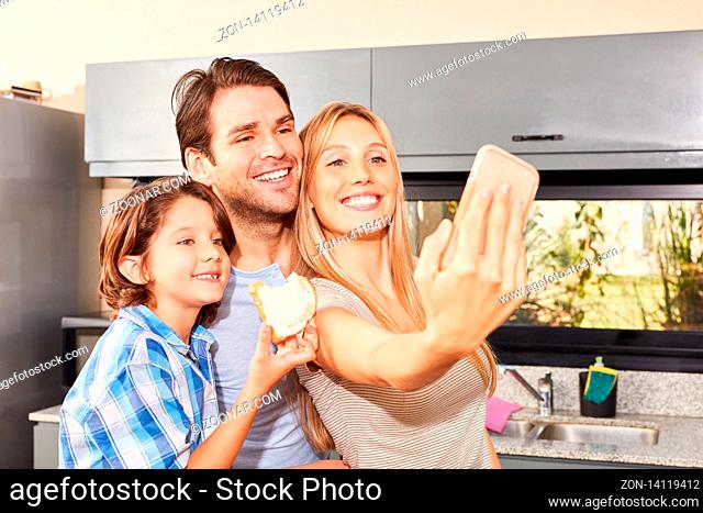 Eltern und Sohn in der Küche beim Frühstück machen ein Selfie mit dem Smartphone