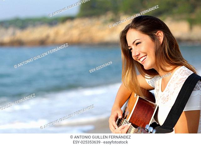 Beautiful guitarist woman playing guitar on the beach with the sea in the background
