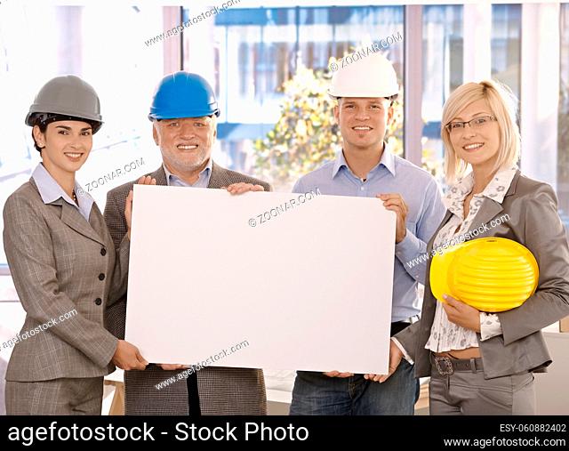 Architect team in hardhat holding blank poster for copyspace in office, smiling