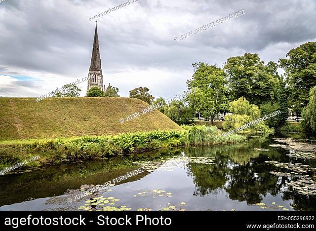 Water pond and church tower in Churchill Park in Copenhagen. It is a public park near Kastellet, a 17th-century fortress