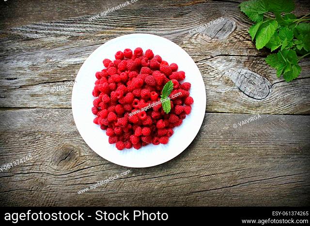 Raspberry fruits in plate on old cutting board, healthy pile of summer berries on grey wooden background, . selective focus