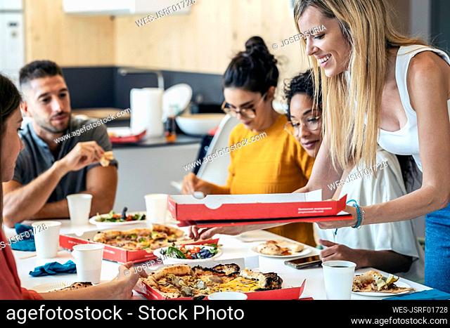 Smiling businesswoman with pizza box by colleagues in lunch break