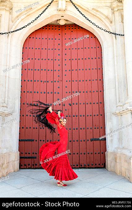 Female flamenco artist with hands raised dancing on footpath