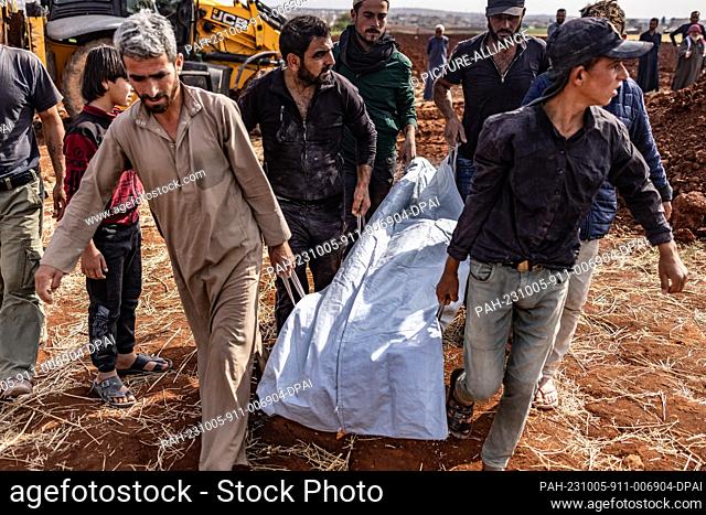 05 October 2023, Syria, Aleppo: People carry the body of a person who was killed during a missile strike that targeted a civilian home in the town of Kafr...