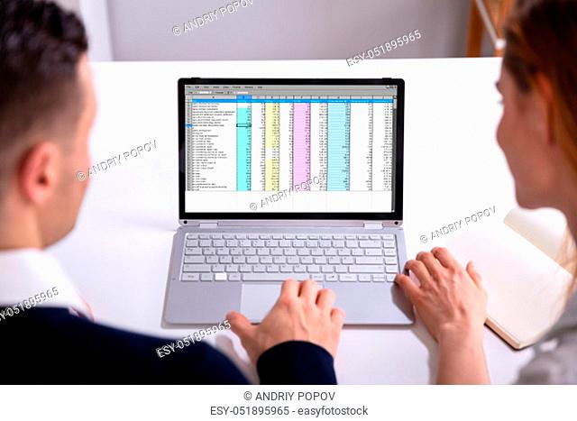 Male And Female Businesspeople Checking Spreadsheet On Laptop Screen Over Desk