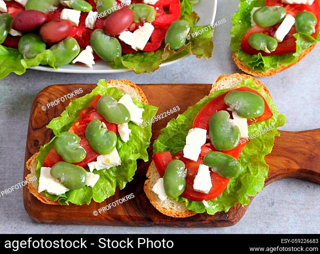 Sandwiches with broad beans, tomatoes and goat cheese. Salad in a bowl