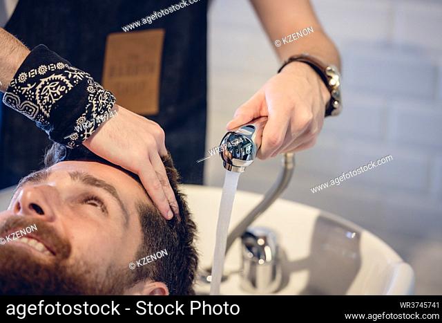 Close-up of the hands of a skilled male hairdresser, giving a hair wash to a happy customer before or after haircut in a modern beauty salon