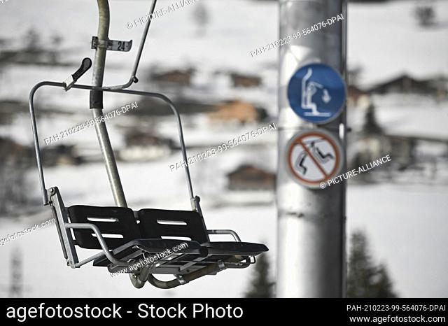 23 February 2021, France, Notre-Dame-De-Bellecombe: An empty chairlift hangs in front of a column with warning signs. Due to the Corona measures