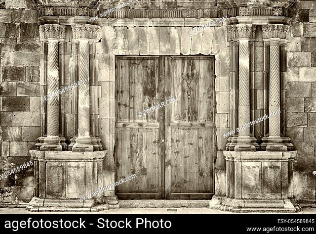 monochrome sepia ancient wooden double doors in an old stone building with crumbling ornate columns surrounding the entrance