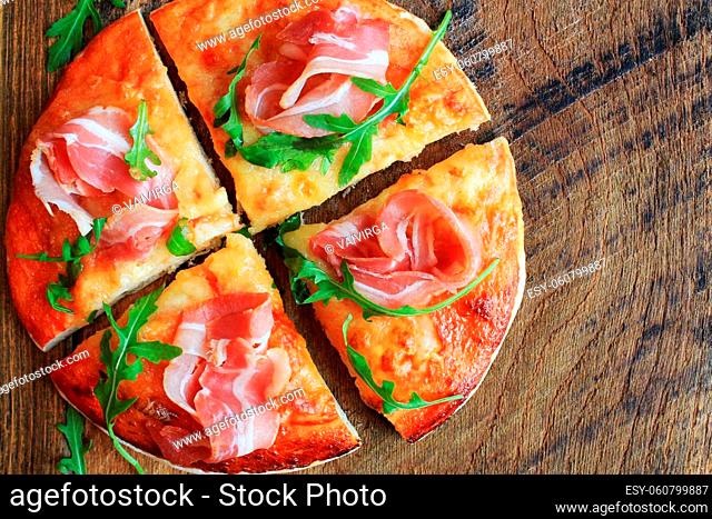 Pizza with smoked ham and rucola on wooden background