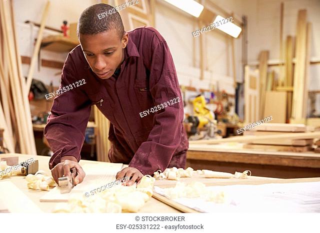 Apprentice Planing Wood In Carpentry Workshop