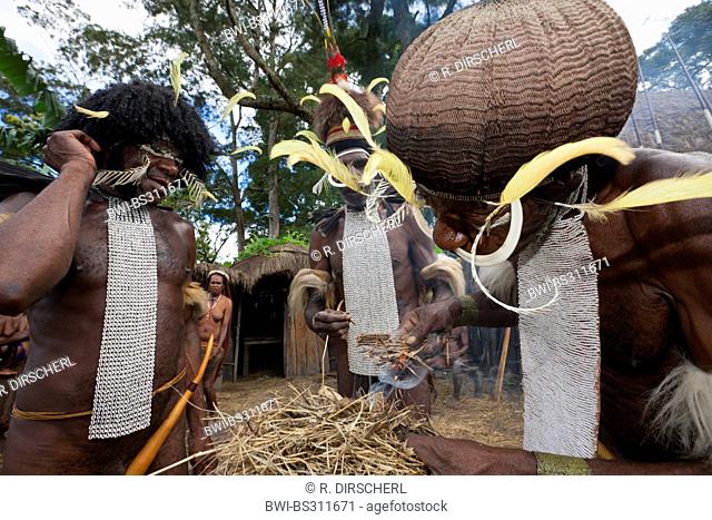 three Dani men making fire in the traditional way under the eyes of the tribe during the rare pigs feast, the pinnacle of the social and religious life