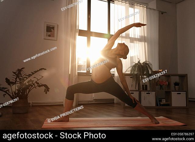 pregnant woman doing yoga at home over sunshine