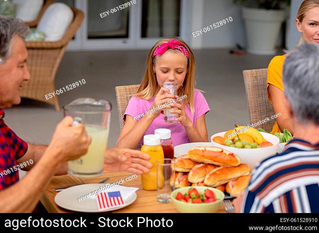 Smiling caucasian girl drinking lemonade sitting with family eating meal together in garden