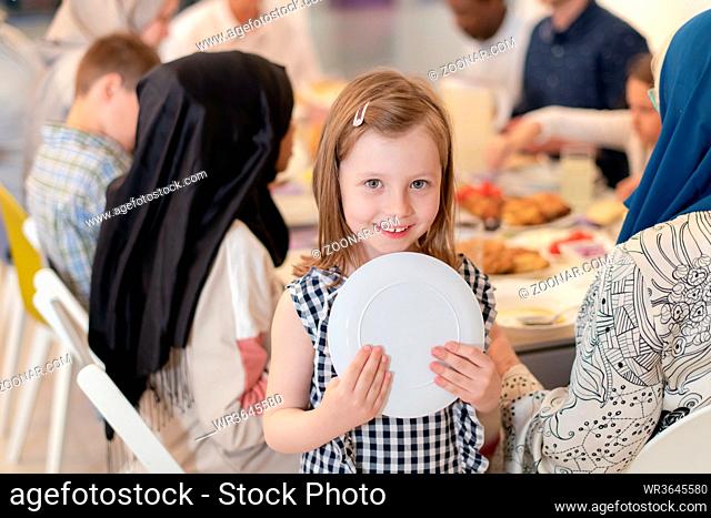 cute little girl enjoying iftar dinner together with modern multiethnic muslim family in the background during a ramadan feast at home