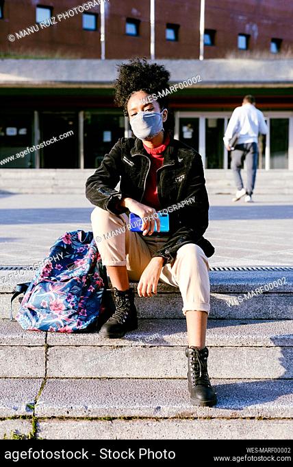 Young woman wearing protective face mask sitting on staircase in city