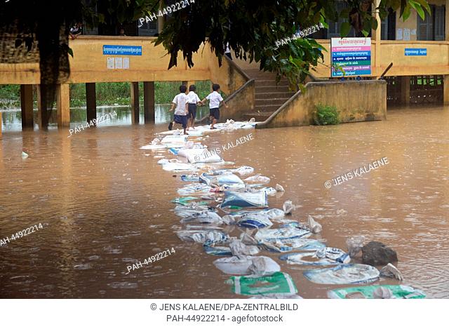 Pupils walk over sand bags in front of the flooded Krom Preah Sandach Primary School in Phnom Penh, Cambodia, 12 October 2013