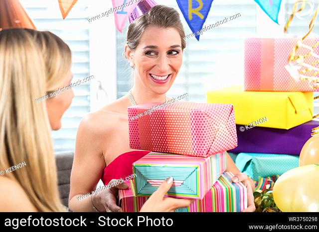 Portrait of a cheerful and beautiful woman smiling at her best friend surrounded by various presents and multicolored party decorations for her birthday
