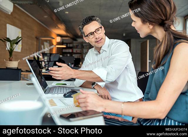 Businessman explaining to colleague while sitting at workplace