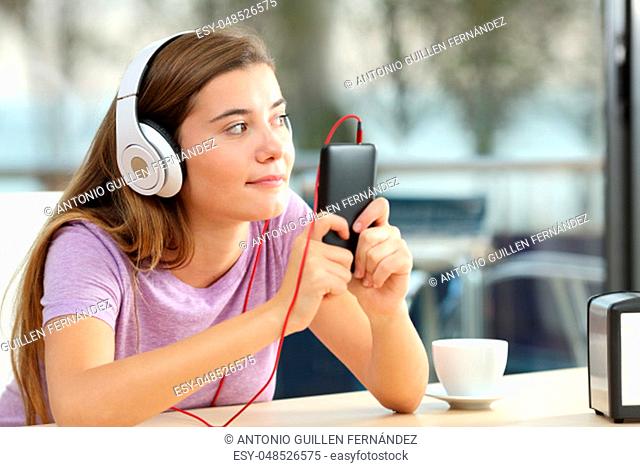 Single teen wearing headphones listening to music from a smart phone in a coffee shop terrace