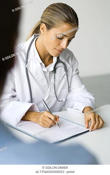 Doctor writing at desk, patient in foreground