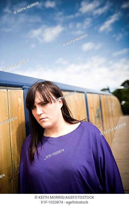 Sad depressed young overweight woman standing on walkway bridge