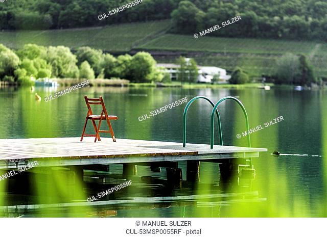 Chair on wooden pier in still rural lake