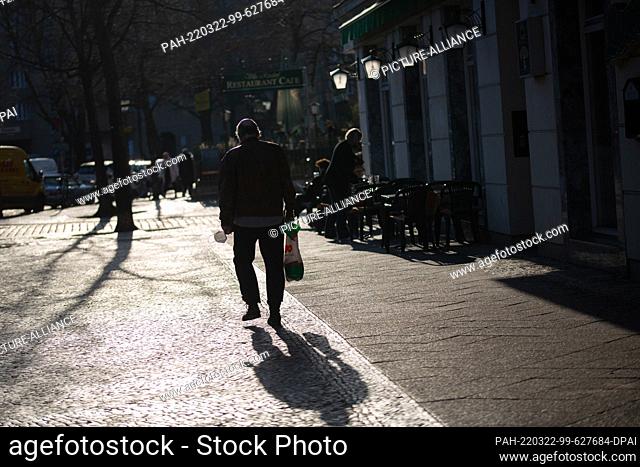 21 March 2022, Berlin: A man walks in the backlight with a mouth-nose protection and a shopping bag in his hands. Photo: Fernando...