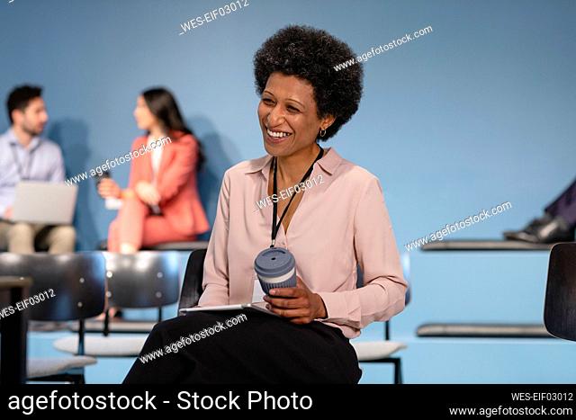Happy businesswoman with disposable coffee cup in office