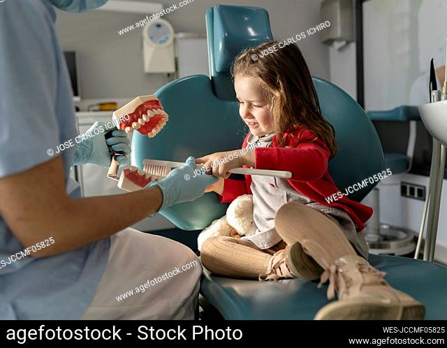Dentist teaching little girl oral hygiene on dentures at dental clinic