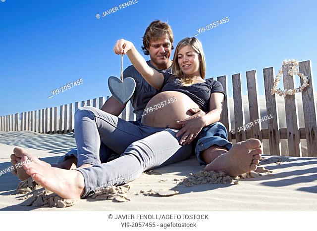 A pregnant woman and her partner sitting on the beach