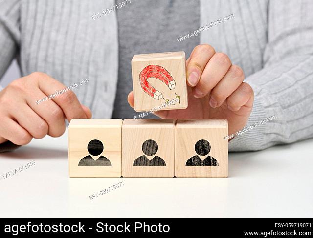 female hand holds a wooden cube with a magnet over the cubes with little men, recruiting for a strong team. Open vacancies in the company