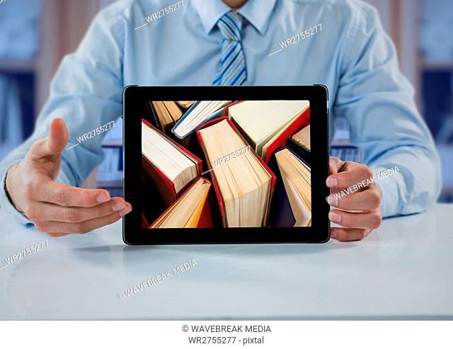 Business man at table with tablet showing standing books against blurry bookshelf with blue overlay