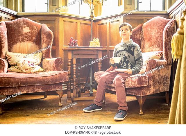 England, Gloucestershire, Thornbury. A young boy sitting in a chair in Thornbury Castle