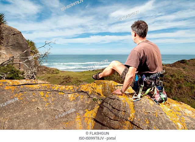 Rock climber at top of rock taking in scenery, Ruapuke, Raglan, New Zealand