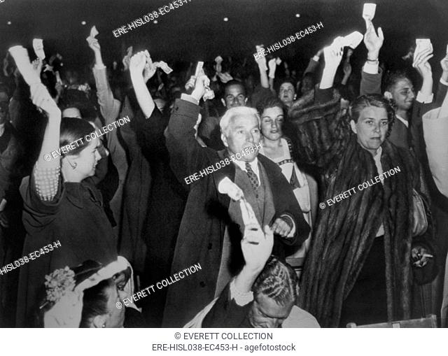 Charlie Chaplin with wife Oona at Hollywood Bowl campaign rally for Henry Wallace in 1948. The audience are holding dollar bills in their hands and Chaplin...
