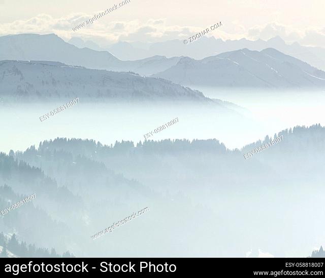 Mountains and mountain ranges with snow in low lying inversion valley fog. Silhouettes of trees and foggy Mountains. Scenic snowy winter landscape