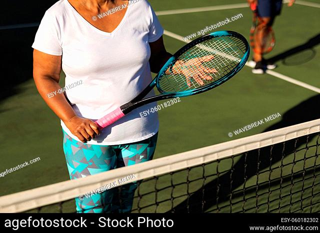 Midsection of senior african american woman holding tennis racket on tennis court